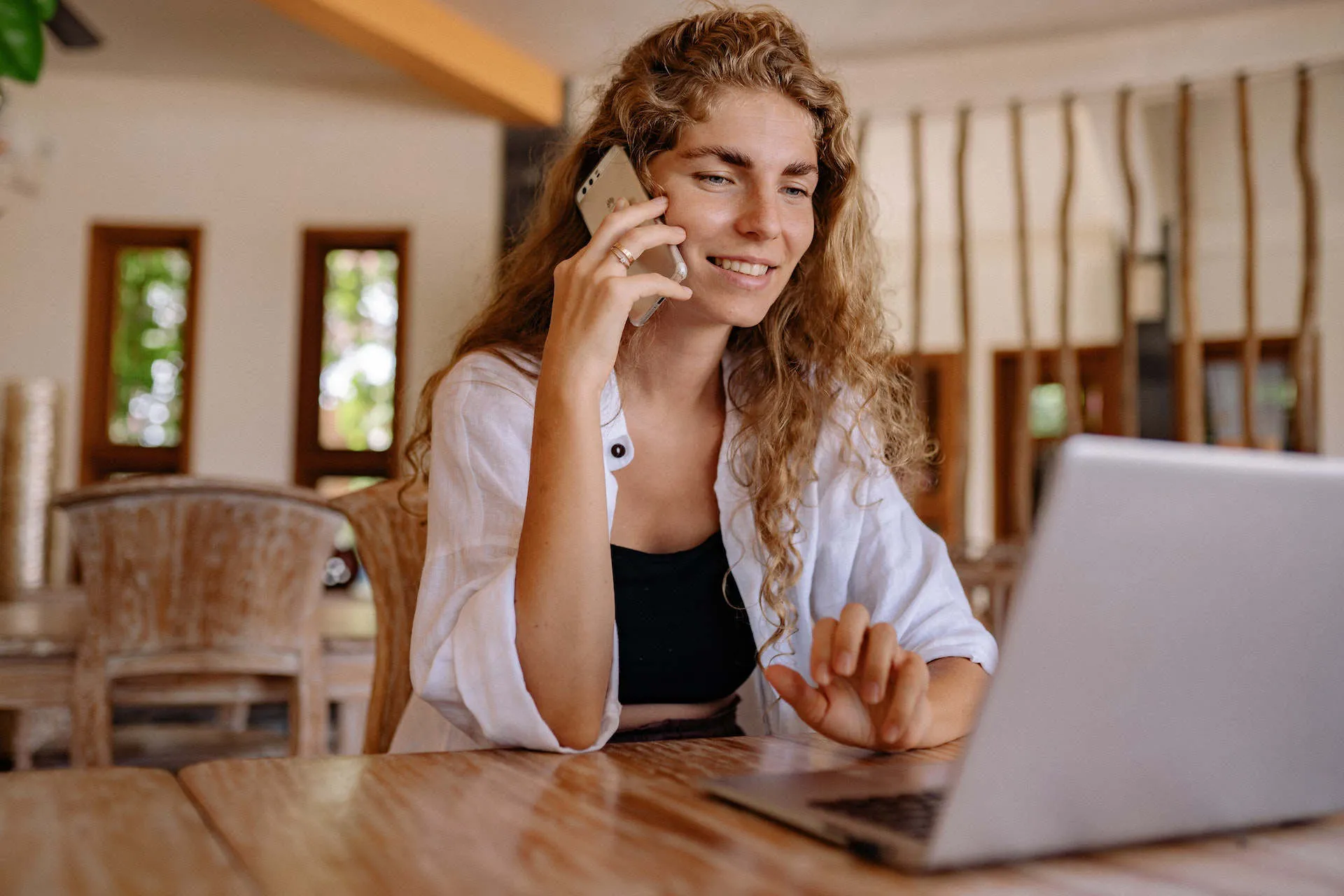 A person at a café table taking a phone call while working at a laptop.